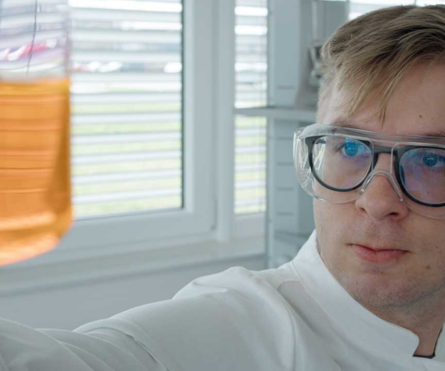 Produktvideo Hannover - Mitarbeiter von Anton Paar Optotec steht im Labor und betrachtet ein Glas mit orangefarbener Flüssigkeit. Titelbild des von 52° Film produzierten Werbefilms für das Cora 5001.
