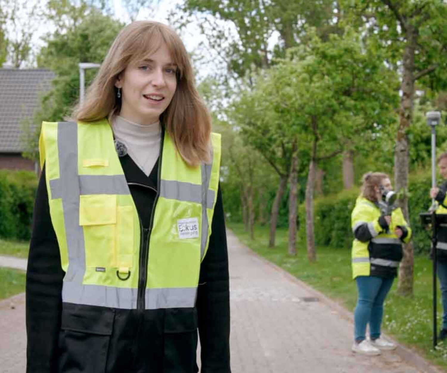 Eine Frau schaut in die Kamera, im Hintergrund Kolleginnen und Kollegen von Fokus Vorsorge mit Messtechnik. Recruitingvideo Hannover von 52° Film.