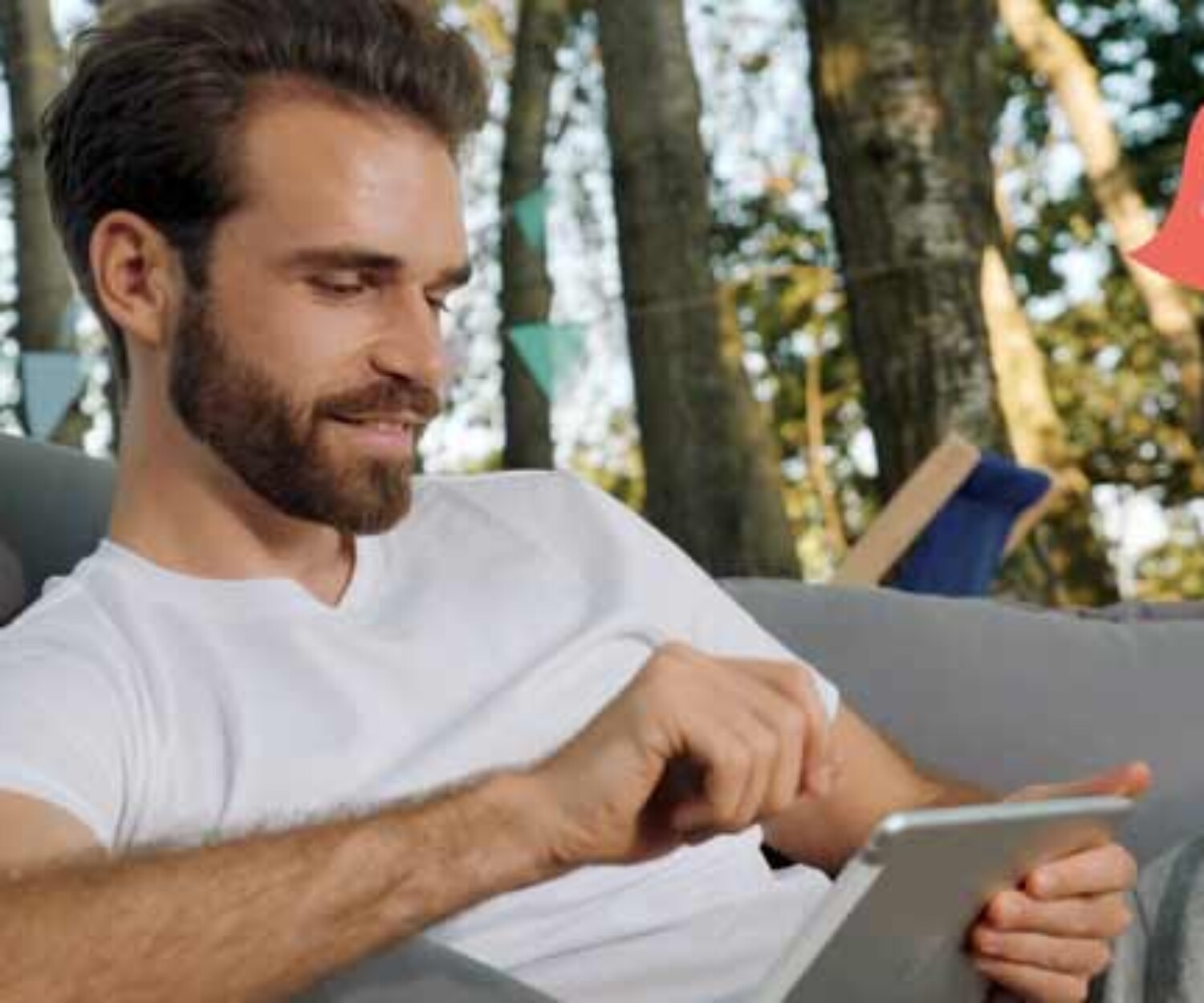 Junger bärtiger Mann sitzt im Sitzsack in der Natur und arbeitet am Tablet – Titelbild eines Recruitingvideos von 52° Film, Filmproduktion Hannover